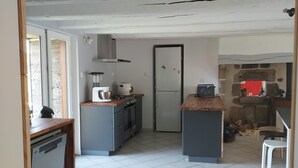 Une cuisine équipée d’un lave-vaisselle, d’une cuisinière et d’un réfrigérateur. Une porte donne accès à une autre pièce.