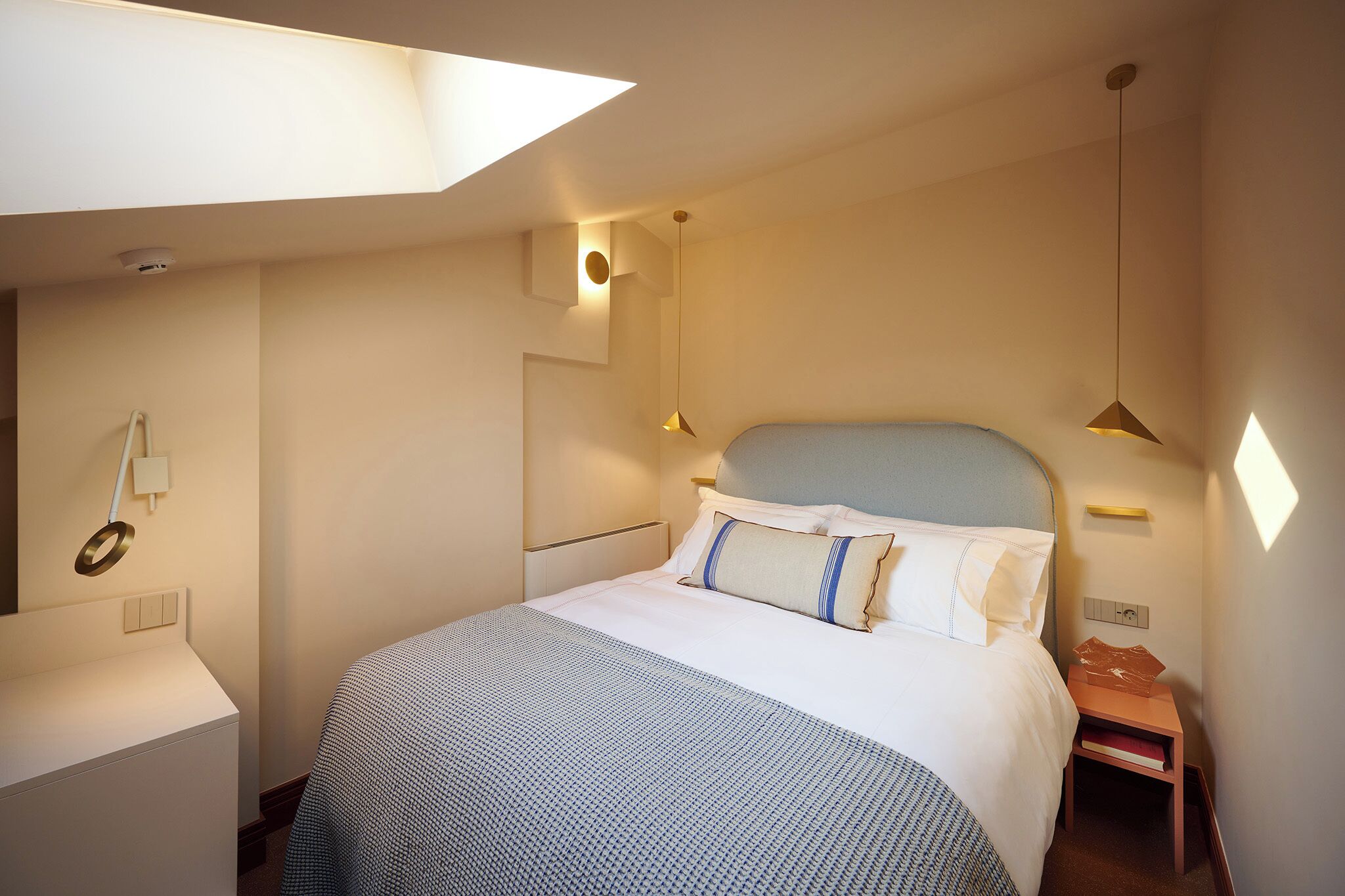 A hotel room with a bed, bedside table, and a small nightstand.