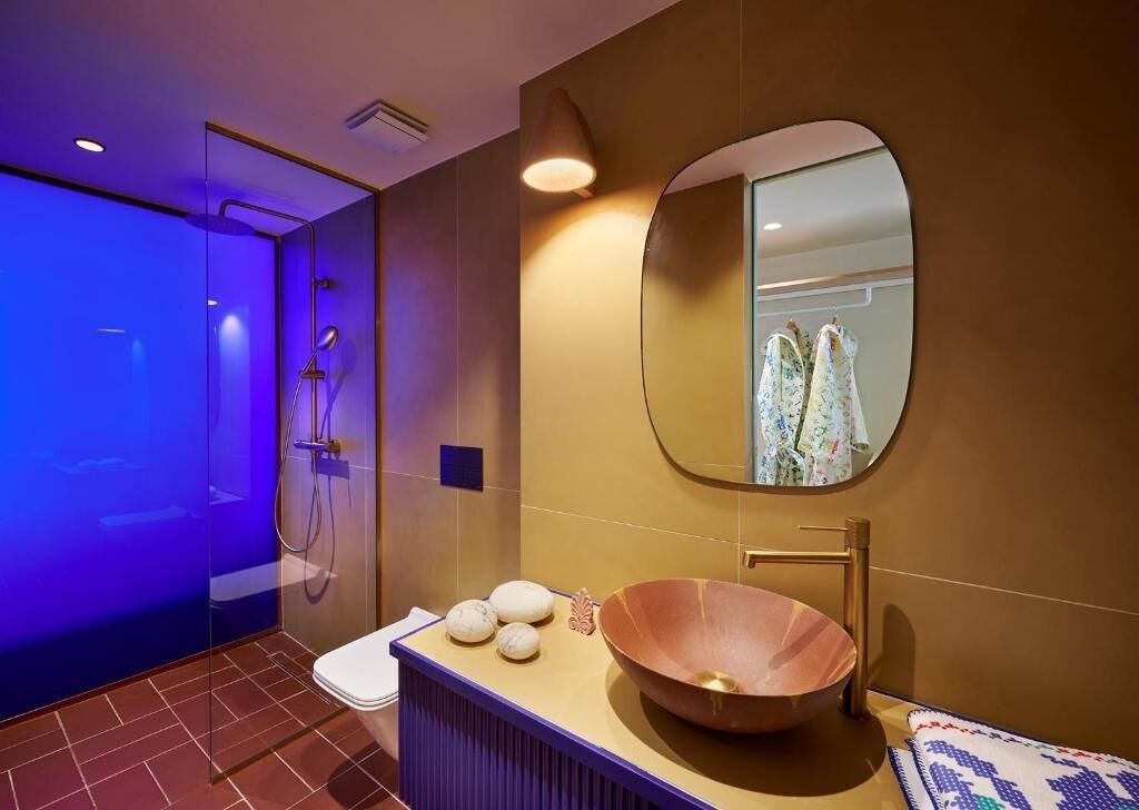 Un baño moderno con cabina de ducha de vidrio, un espejo redondo, lavamanos de madera y un inodoro.