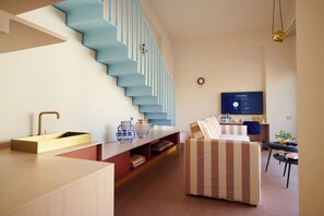 A modern living room with a staircase, a sofa, a TV, and a small table with a plant. - Loom Athens (Athens)