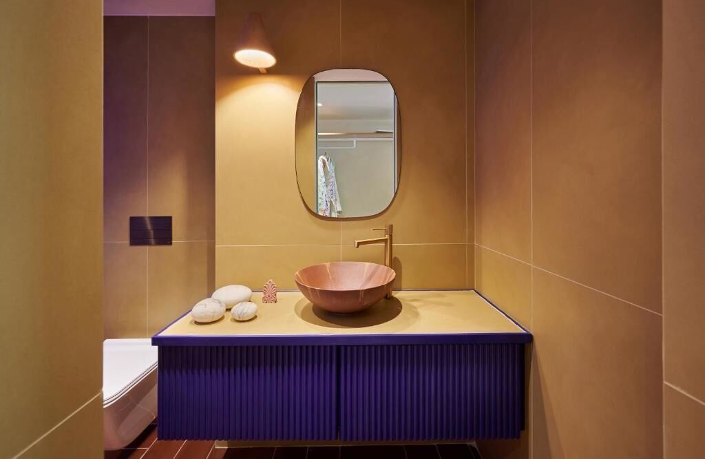 A bathroom with a large oval mirror, a wooden bowl sink, and a blue vanity.