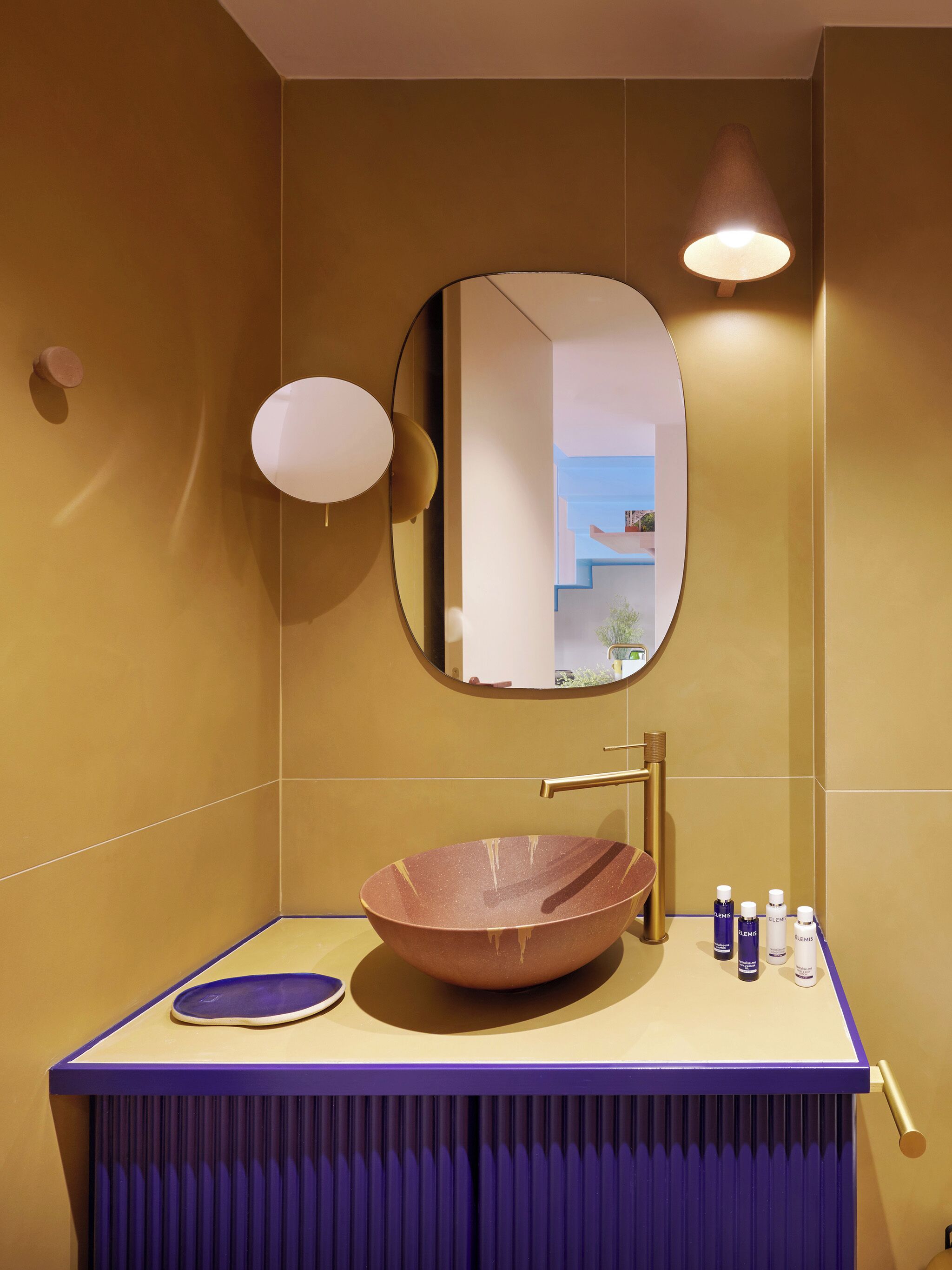 Un baño con un espejo redondo, un lavabo de cobre y artículos de aseo en la encimera.