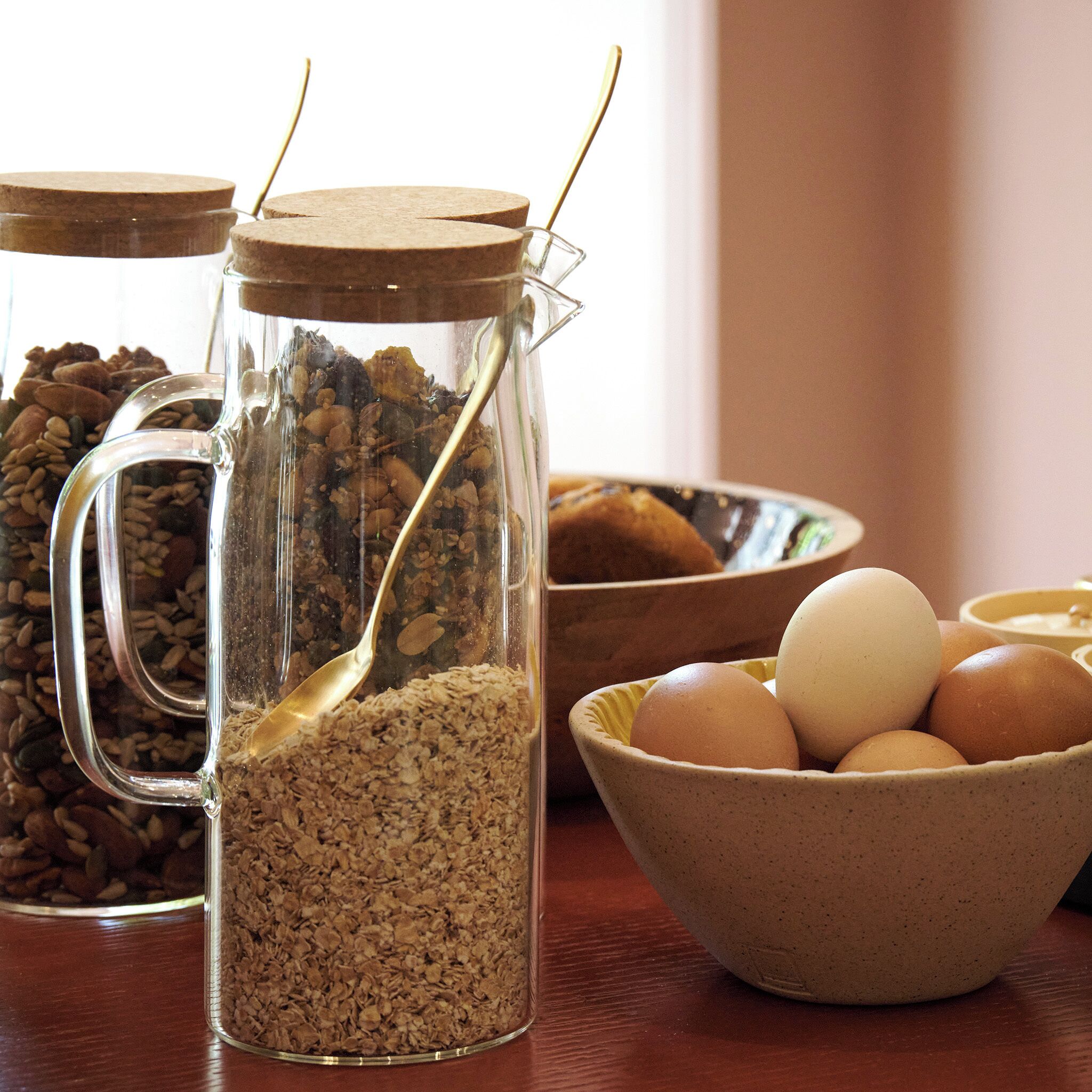 A kitchen with a glass jar filled with oats and a spoon, a bowl of eggs, and a container of coffee beans.