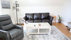 Una sala de estar con un sofá de cuero negro, un sillón a juego, una mesa de centro blanca y una alfombra estampada.