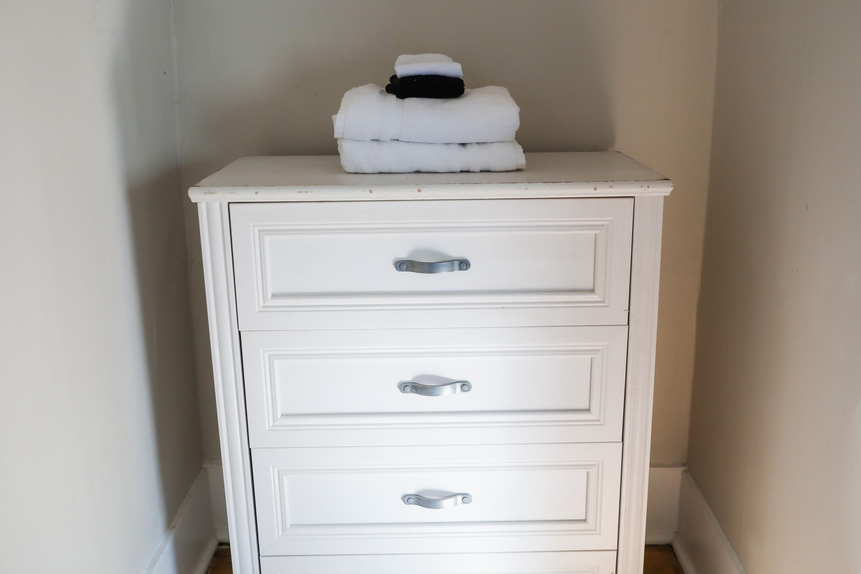 A white dresser with three drawers and a stack of white towels on top.