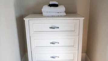 A white dresser with three drawers and a stack of white towels on top.