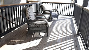 Una terraza de madera con mobiliario de mimbre y barandilla negra.