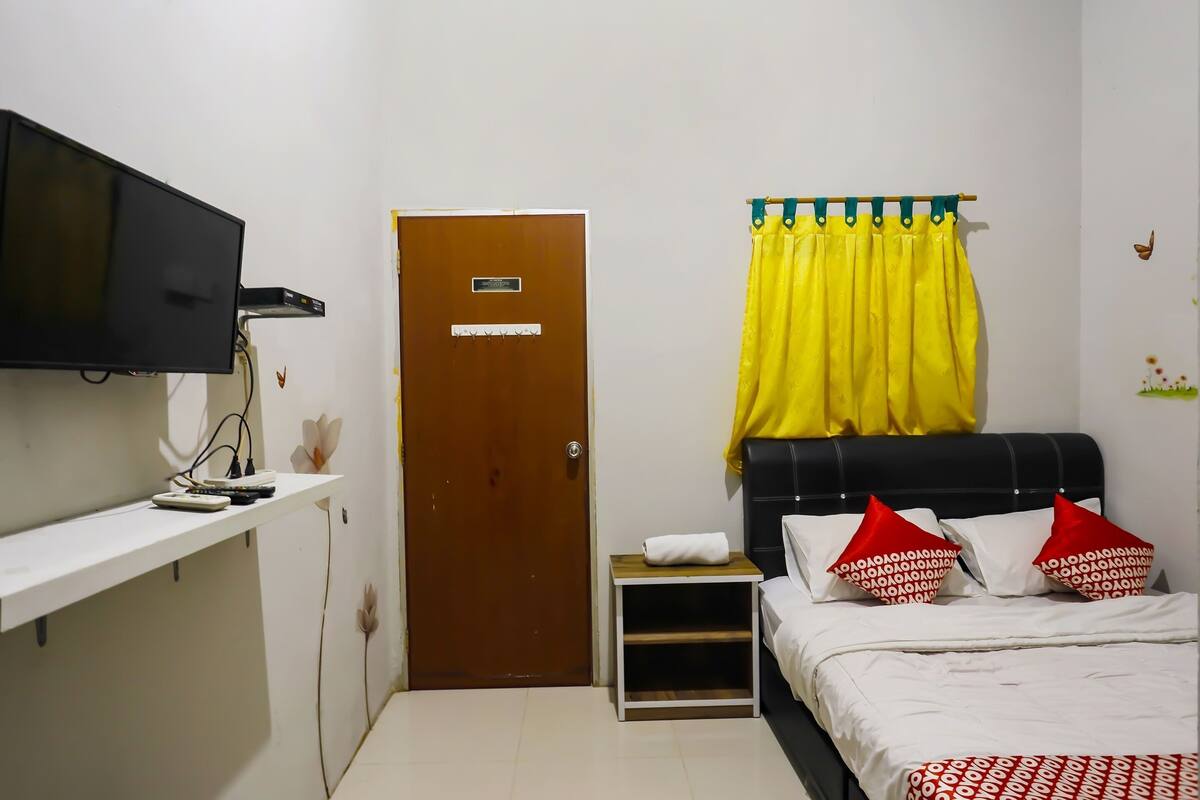 A bedroom with a bed, a TV mounted on the wall, a door, and a small bedside table.