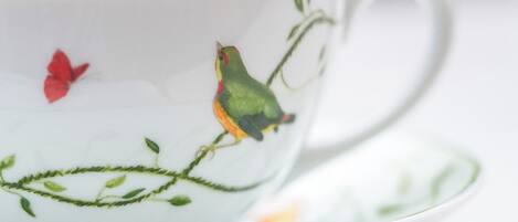 A white ceramic cup with bird and leaf designs, placed on a white saucer.