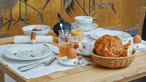 A dining table with plates, cutlery, a basket of bread, and a glass of juice. - L'Absinthe Hôtel (Honfleur)
