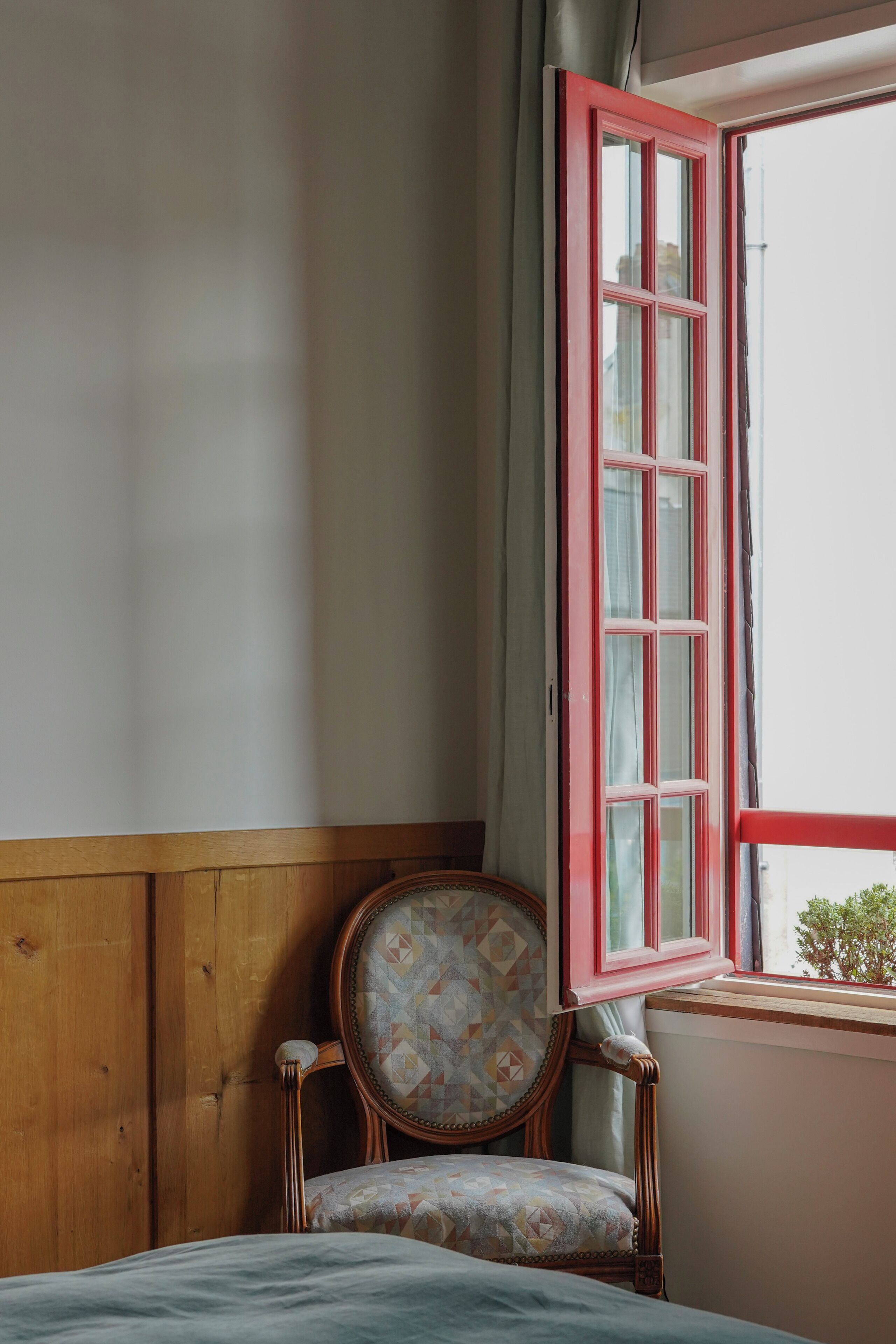 Una stanza con parete rivestita in legno, una sedia decorata e una finestra con stipiti rossi.