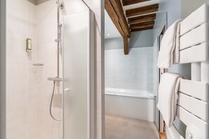 A modern bathroom with a glass shower enclosure, a white bathtub, and a wooden ceiling beam. - L'Absinthe Hôtel (Honfleur)