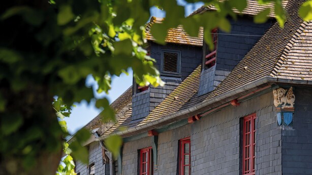 A traditional stone building with red doors and windows, featuring a cobblestone street and a tree in the foreground. - L'Absinthe Hôtel (Honfleur)