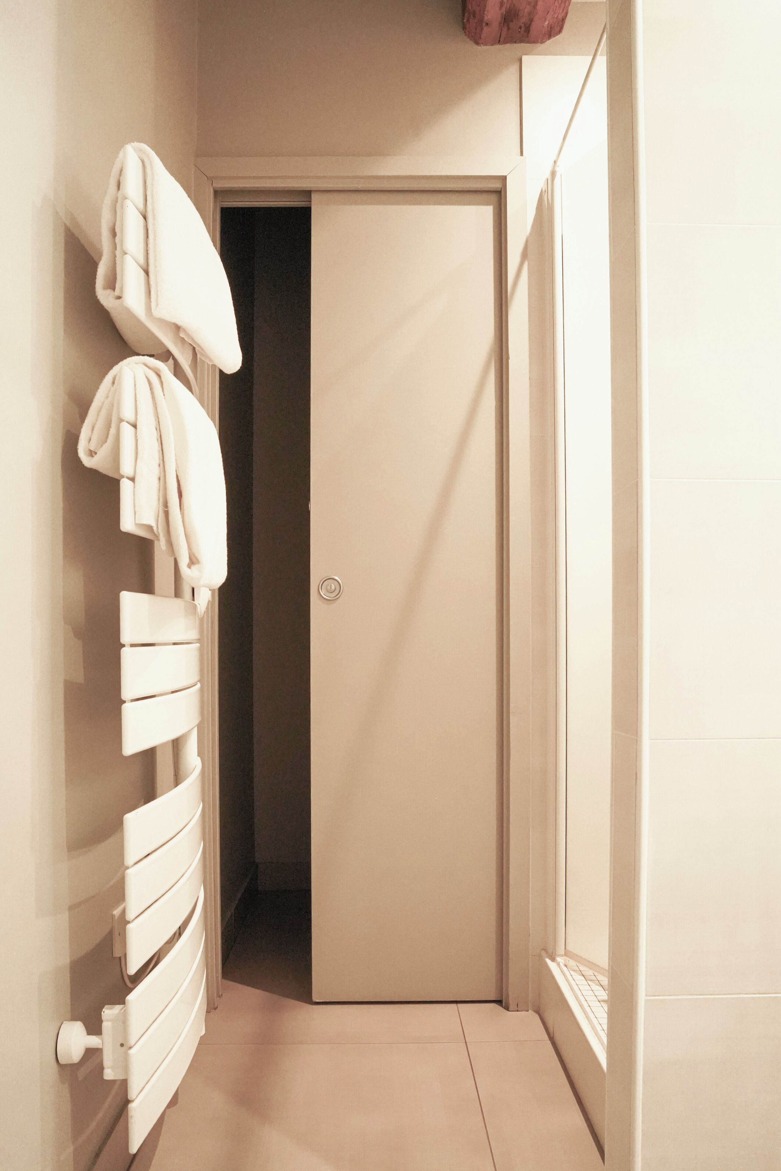 A narrow hallway with a radiator, a towel rack, and a closed door at the end.