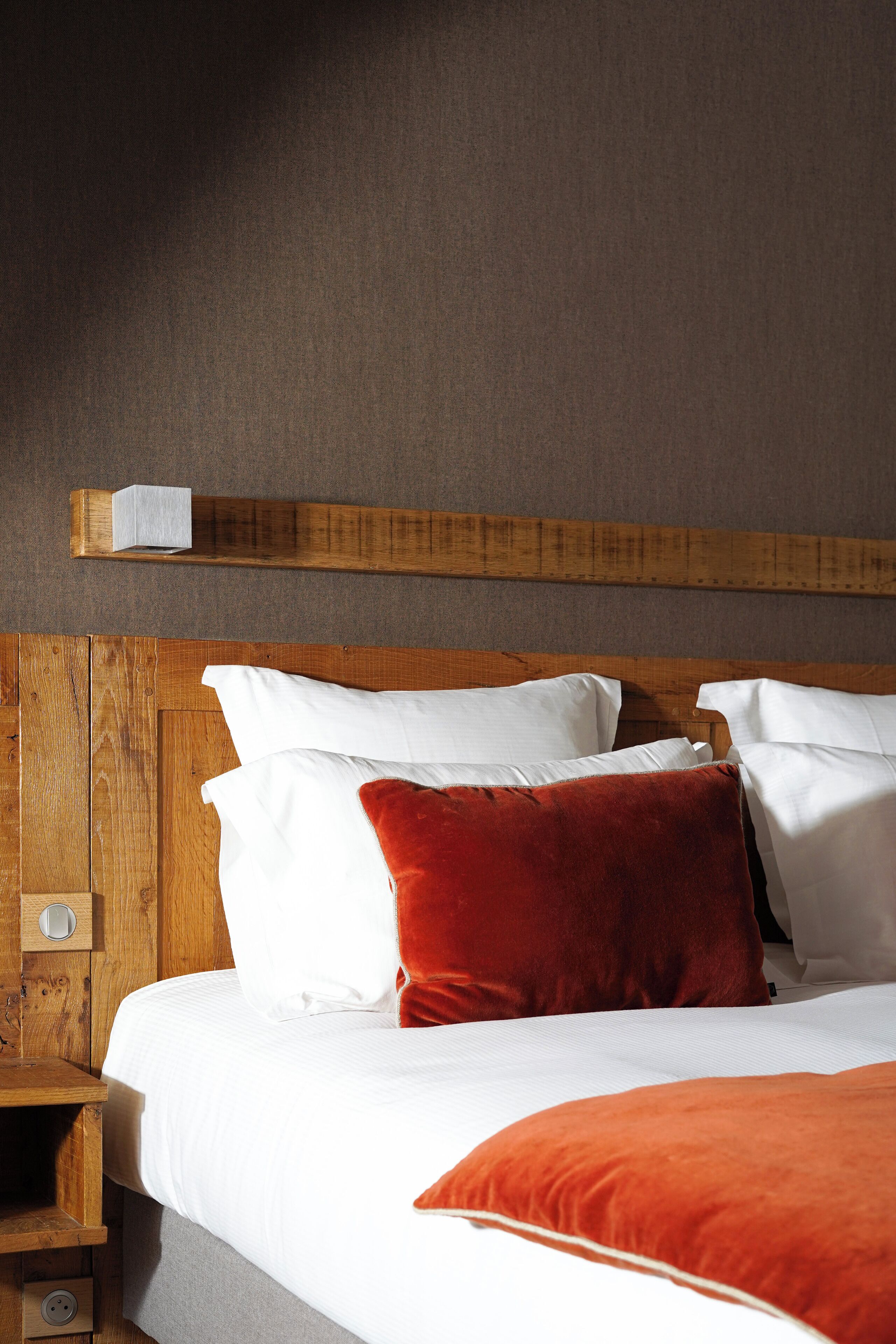 Una cama bien hecha con almohadas blancas y rojas, un cabecero de madera y una mesita de noche de madera con una lámpara.