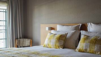 A neatly made bed with a checkered pillow, a wooden headboard, and a chair beside the window.