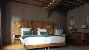Un dormitorio con estructura de cama de madera, ropa de cama blanca y una alfombra gris. Hay una mesita de noche de madera con una lámpara y una pequeña mesa con otra lámpara. El techo es de madera y hay un cuadro enmarcado en la pared.