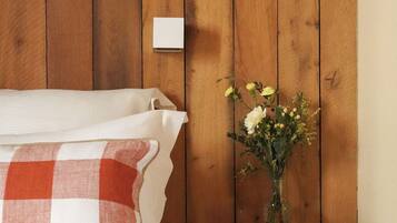 Un dormitorio con cabecera de madera, colcha a cuadros, almohada blanca, un jarrón con flores y una mesita de noche de madera.
