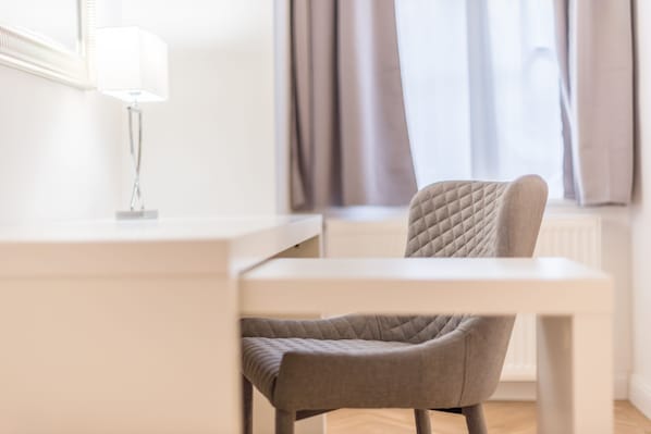 A modern, minimalist room with a white desk, a grey upholstered chair, and a lamp.