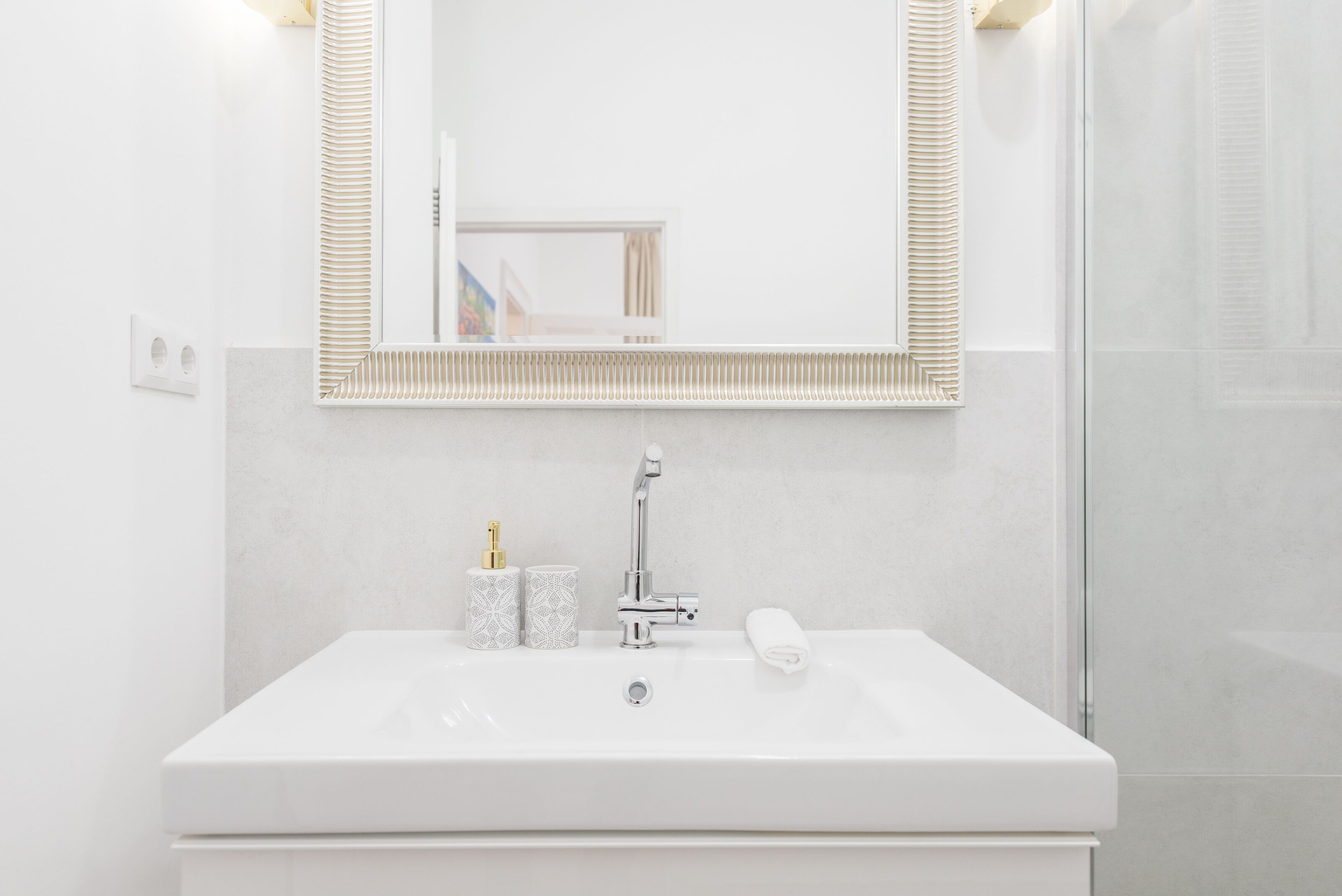 A white bathroom with a rectangular sink, a mirror with a ribbed frame, and a towel on the sink.