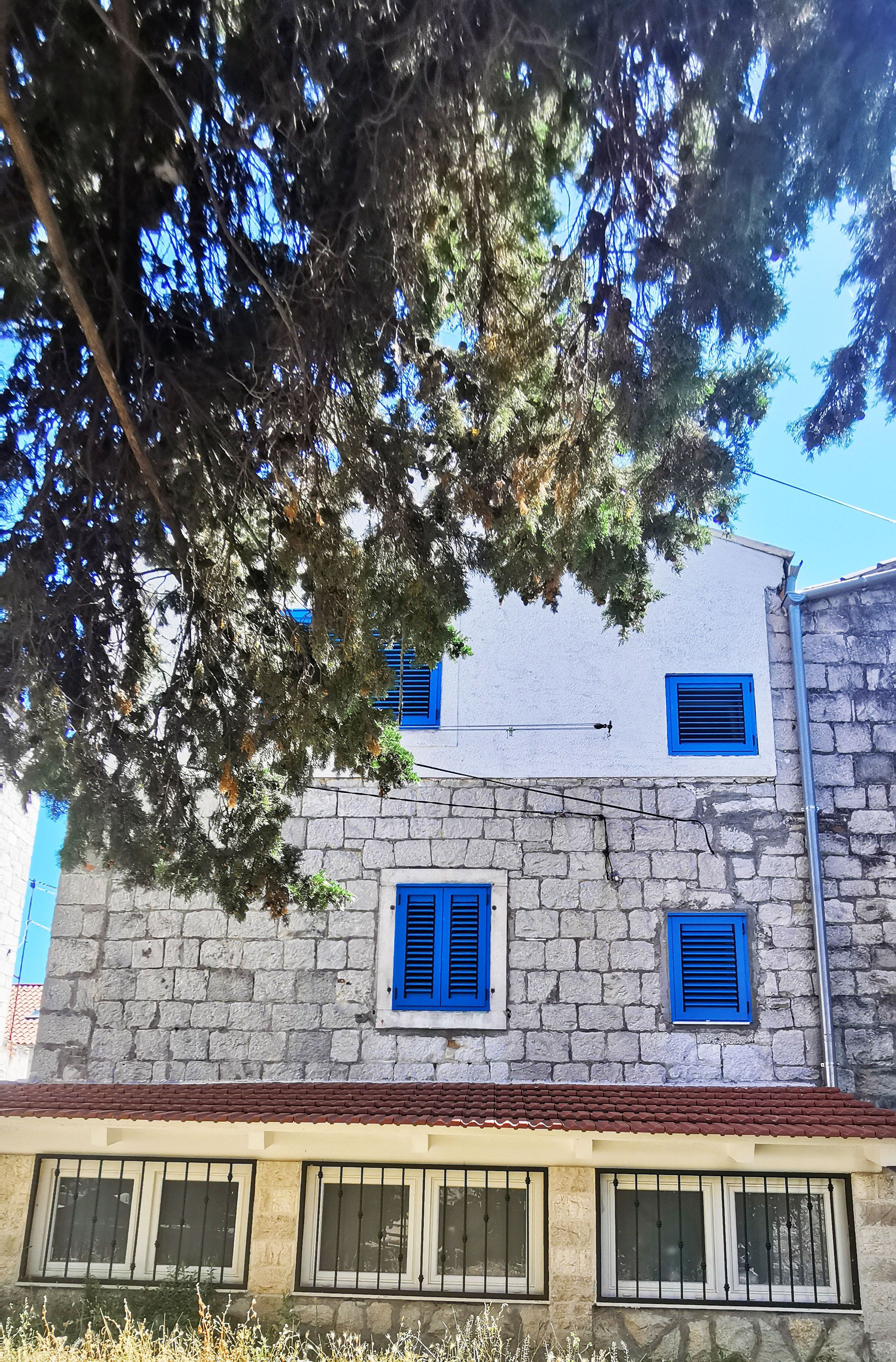 Un edificio de paredes de piedra y contraventanas azules, con numerosas ventanas y tejado de tejas.