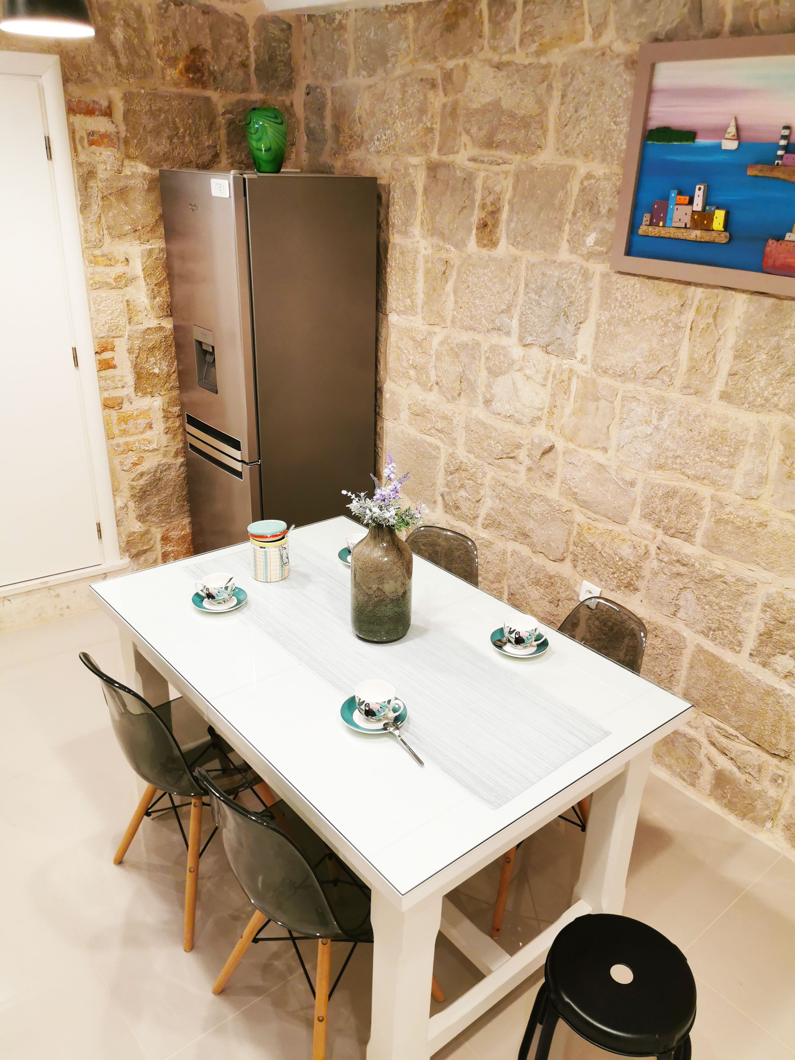 A dining area with a white table, chairs, a vase with flowers, and a refrigerator.