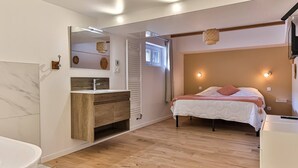 A modern bedroom with a wooden floor, a white bed, a wooden vanity, a large mirror, and a ceiling light fixture.