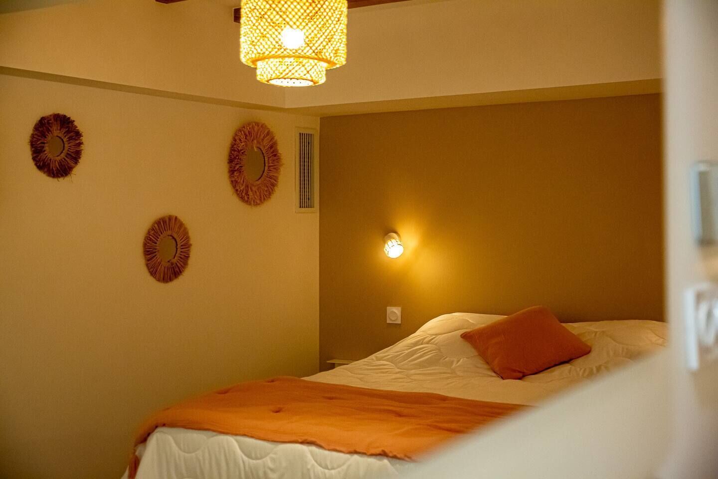 Une chambre à coucher avec un lit, une lampe fixée au mur et des œuvres d’art décoratives accrochées au mur.
