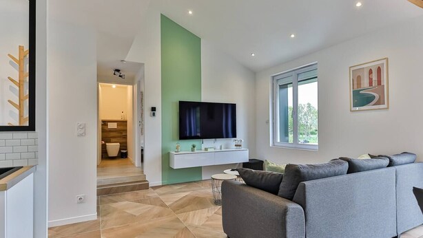 A modern living room with a grey sofa, a mounted TV, and a green accent wall.