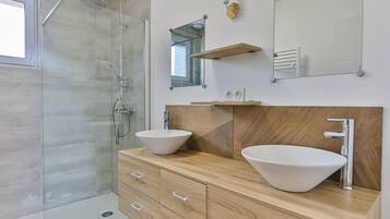 A modern bathroom with two sinks, a shower, and a mirror.