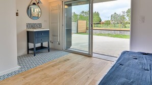 A modern bedroom with a large sliding glass door leading to an outdoor area, a built-in bench, and a small bedside table with a mirror.