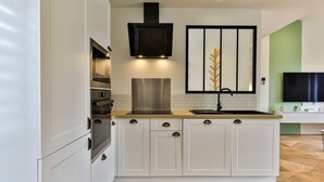 A modern kitchen with white cabinetry, a stainless steel range hood, a built-in oven, and a wooden countertop.