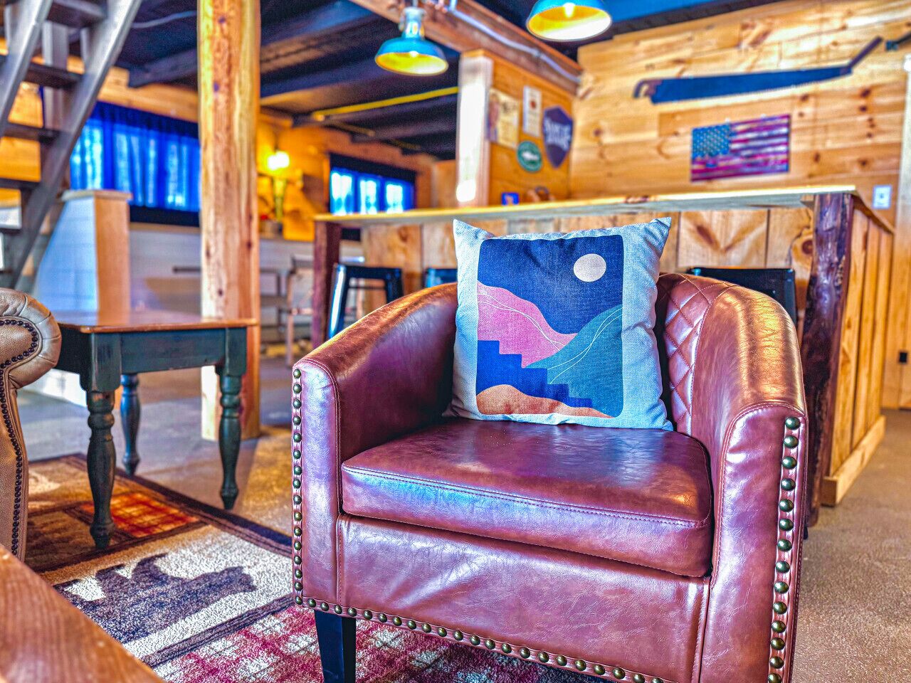 A leather armchair with a colorful pillow in a rustic interior with wooden walls and a wooden staircase.