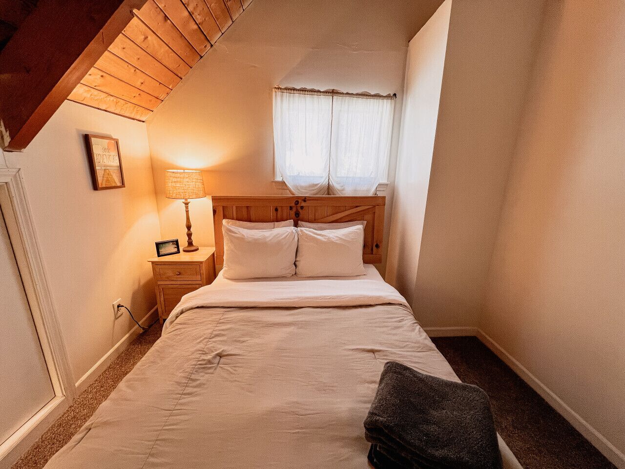 Une chambre à coucher avec une tête de lit en bois, une lampe de chevet, une fenêtre avec des rideaux et un lit soigneusement fait.