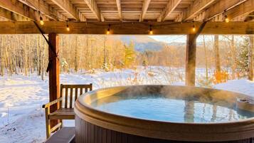 Un jacuzzi bajo una pérgola de madera con un paisaje nevado al fondo.