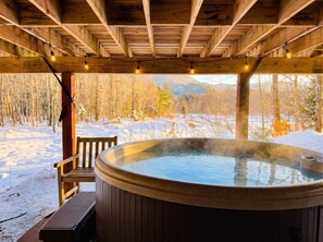 Un jacuzzi bajo una pérgola de madera con un paisaje nevado al fondo.