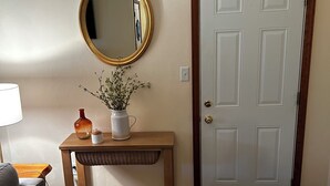 A hallway with a wooden console table, a mirror, a vase with flowers, a door, and a patterned rug.