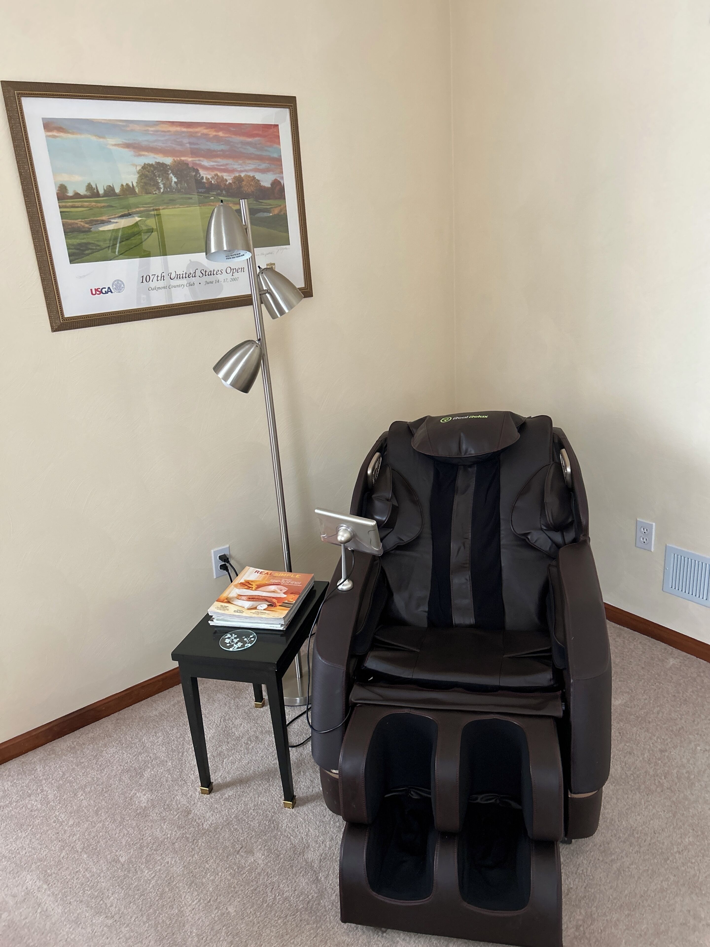 Un fauteuil massant, un certificat encadré et une petite table avec des magazines.