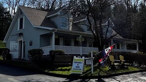 A two-story house with a porch, a sign indicating Building 2 is open, and a flag.