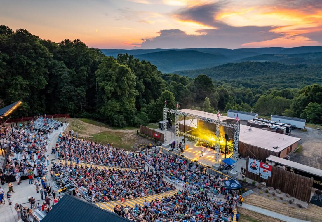 An outdoor amphitheater with tiered seating, surrounded by forested hills.