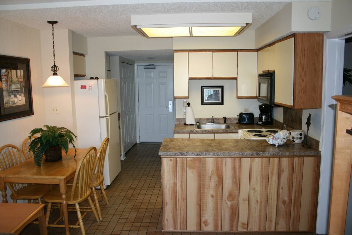 A kitchen with wooden cabinets, a refrigerator, a sink, and a dining table with chairs.
