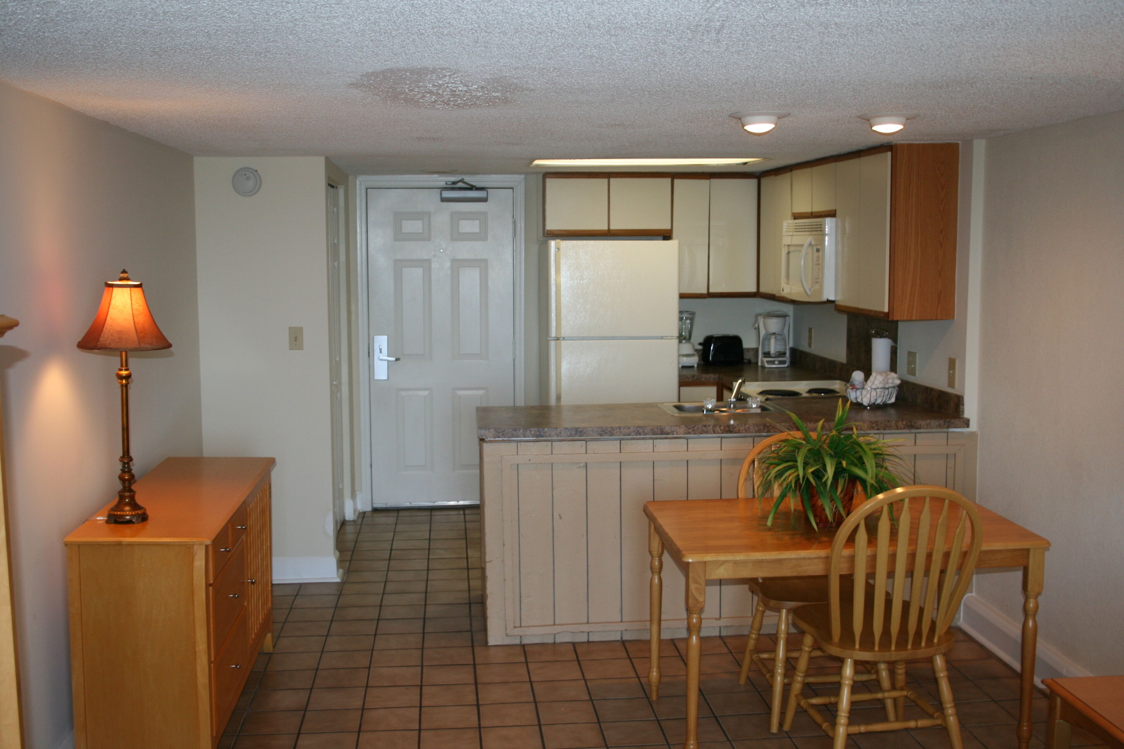 A compact kitchen with a dining area, featuring a refrigerator, coffee maker, and a potted plant on the counter.