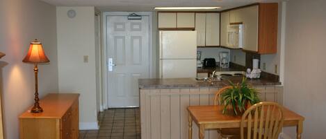 A compact kitchen with a dining area, featuring a refrigerator, coffee maker, and a potted plant on the counter.