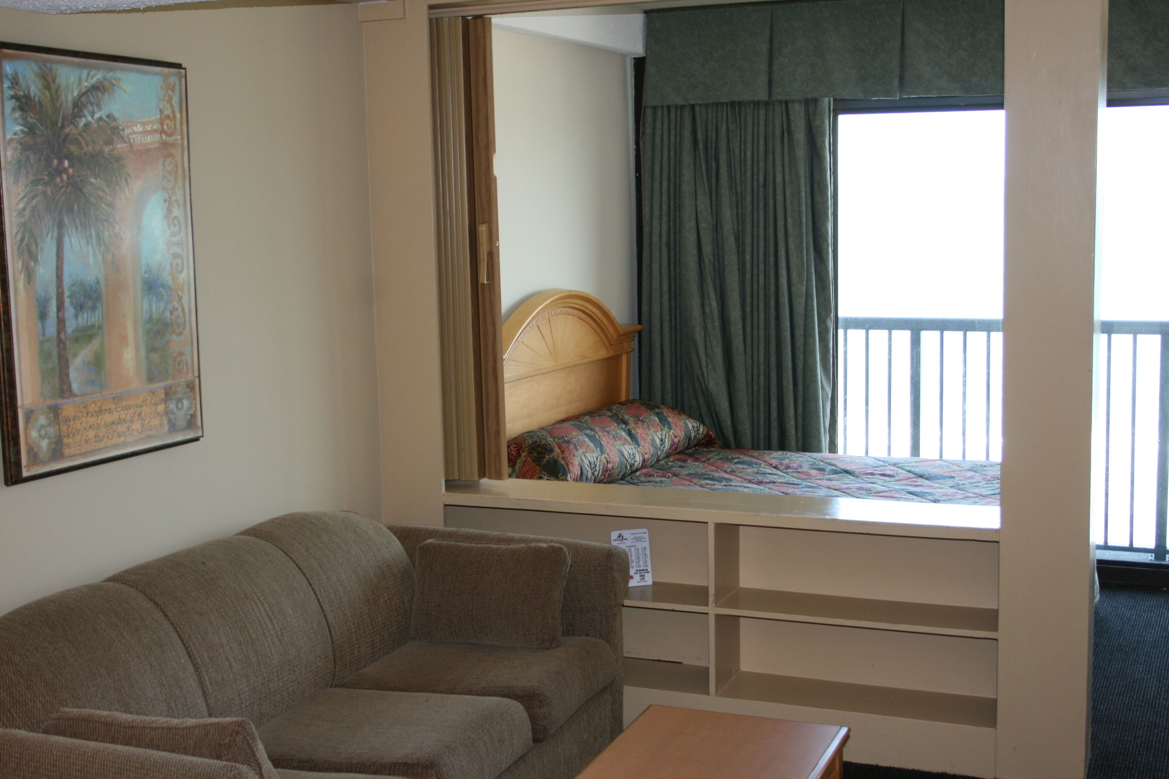 A bedroom with a bed, a headboard, a window with curtains, a couch, and a small table.