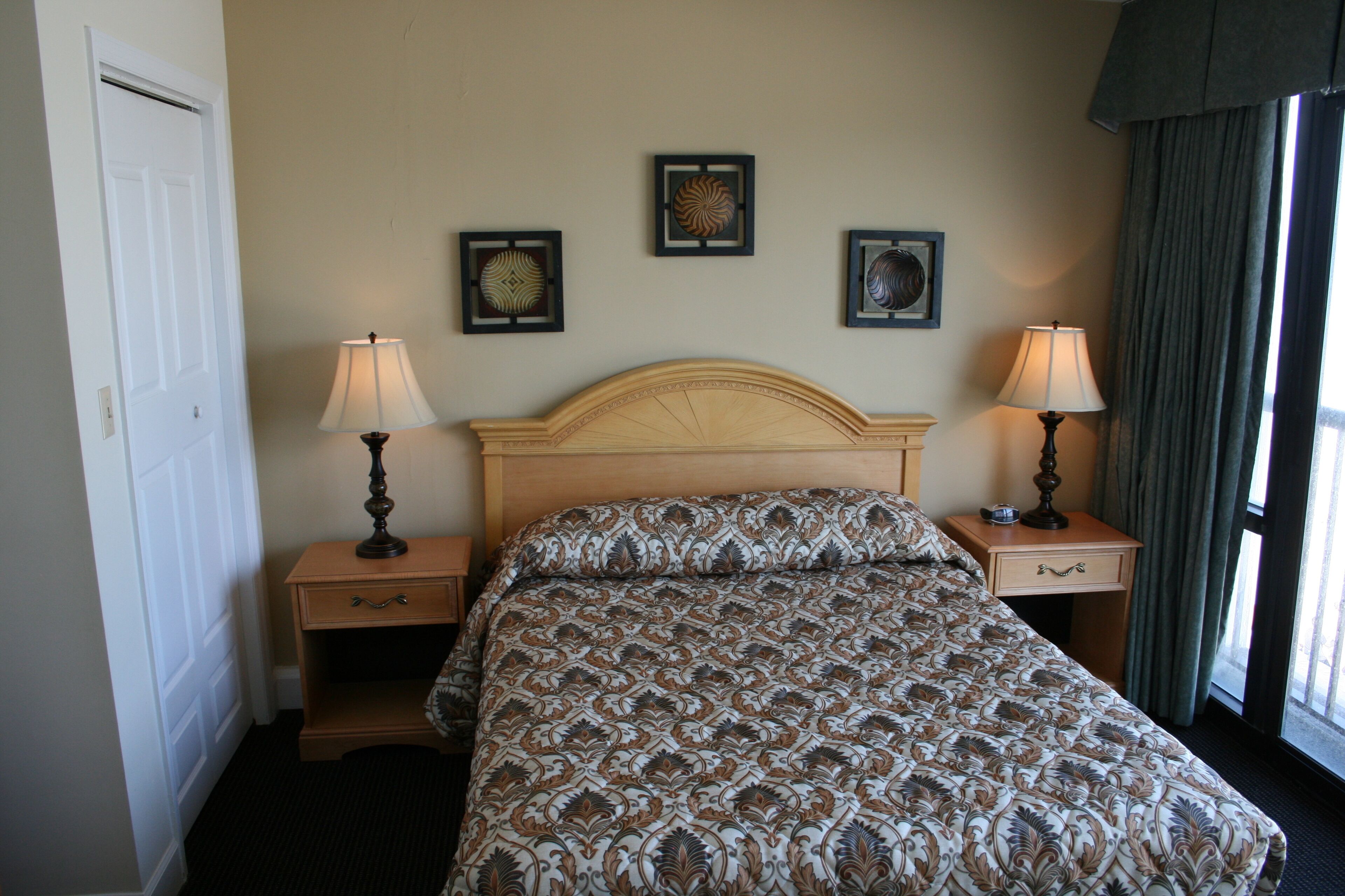 A hotel room with a bed, two bedside tables with lamps, a door, and three framed pictures on the wall.