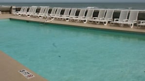 Una piscina amb aigua cristal·lina, un seu de socorrista i una filera de gandules blanques orientades cap al mar.