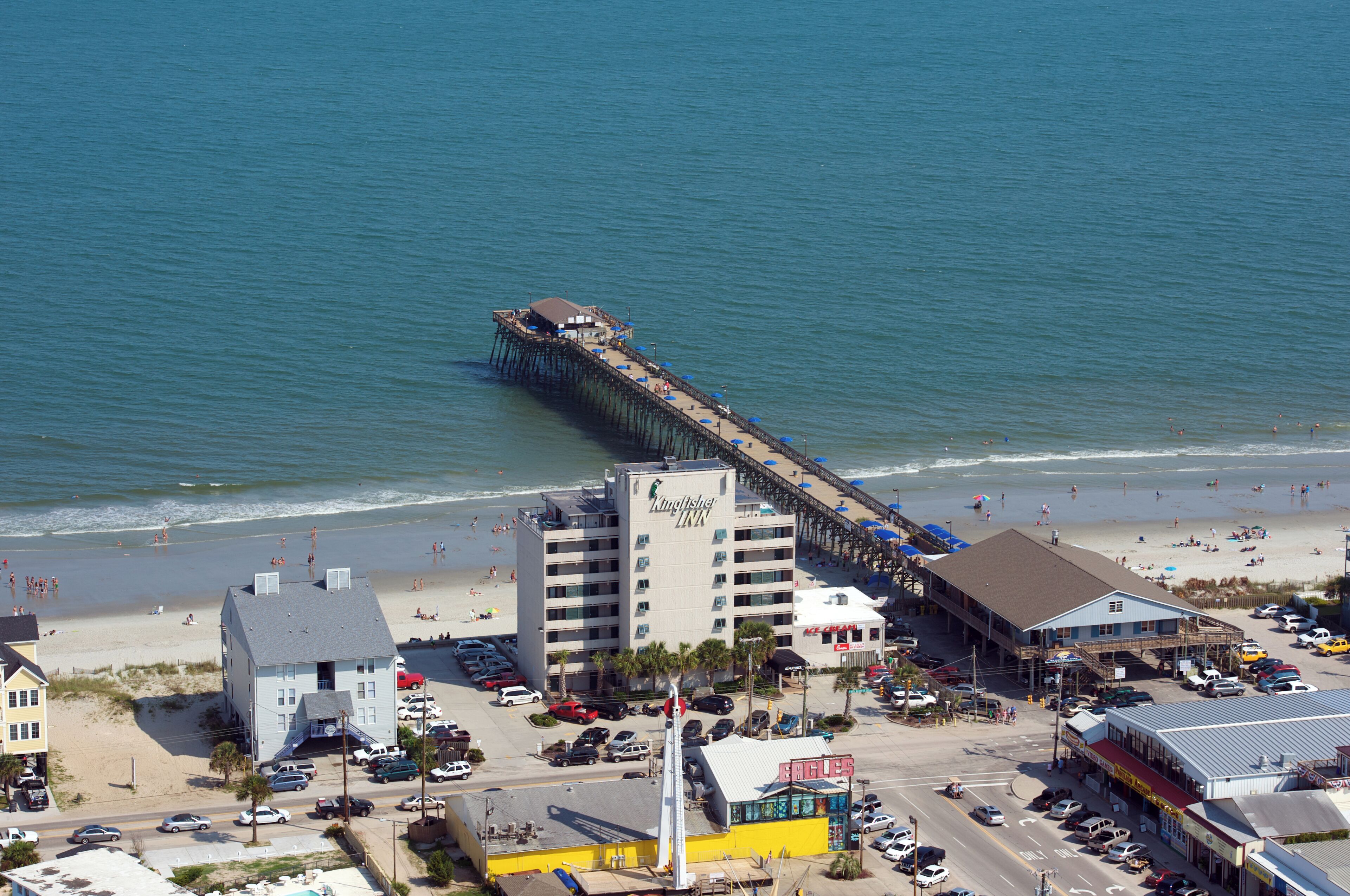 Un muelle que se adentra en el océano, con un hotel y servicios de playa cerca.