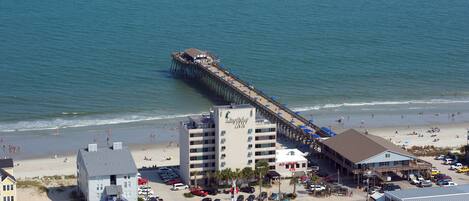 Un muelle que se adentra en el océano, con un hotel y servicios de playa cerca.