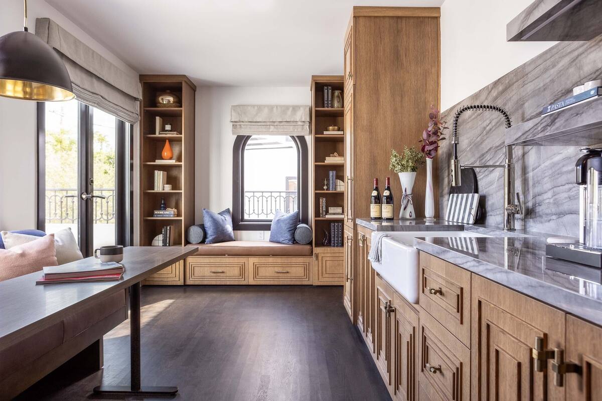 A modern kitchen with wooden cabinets, a marble countertop, and a built-in bench with cushions.