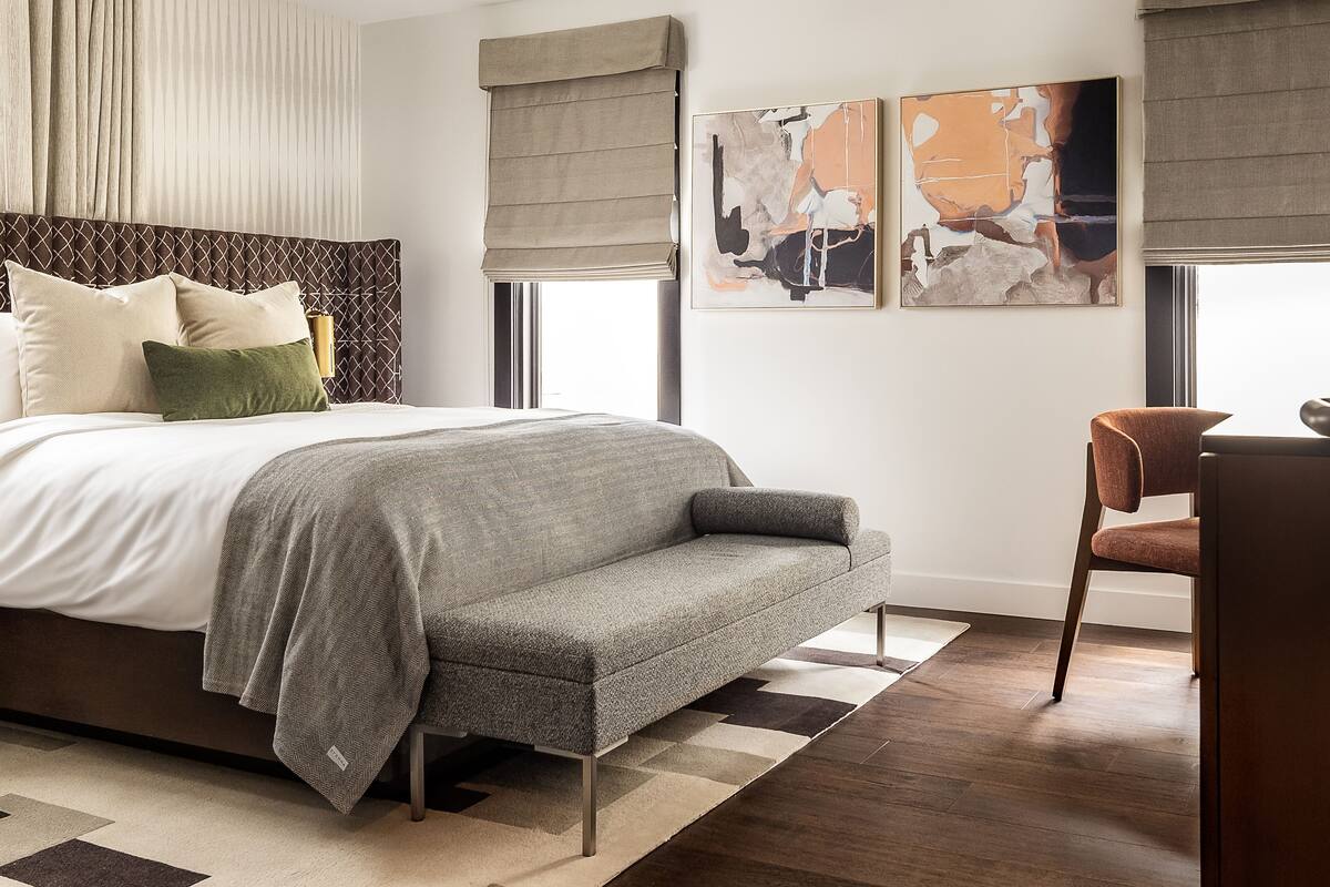 A modern bedroom with a large bed, a sofa, a chair, and abstract wall art.